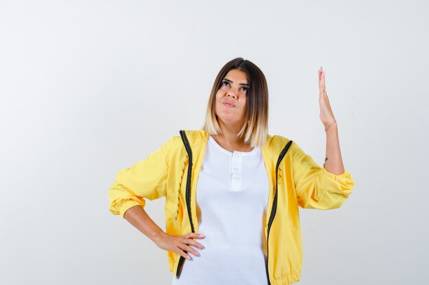 Frau im T-Shirt, Jacke, die Hand hebt, während sie oben schaut und verträumt, Vorderansicht schaut.