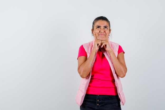 Frau im T-Shirt, Weste, die Finger auf Wangen hält und fröhlich aussieht me