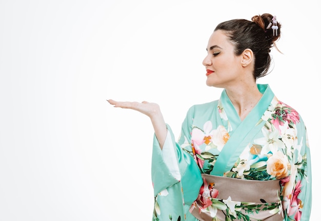 Frau im traditionellen japanischen Kimono, die mit einem Lächeln auf einem glücklichen Gesicht beiseite schaut und etwas mit dem Arm ihrer Hand auf Weiß präsentiert