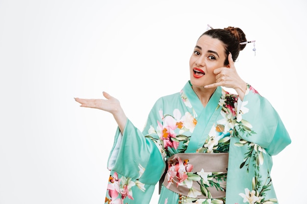 Frau im traditionellen japanischen Kimono, glücklich und positiv, rufen Sie mich an, indem Sie etwas mit dem Arm ihrer Hand auf Weiß präsentieren