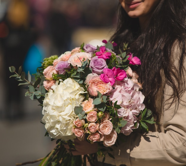 Frau im Trenchcoat, der einen Mischblumenstrauß von Winterblumen hält.