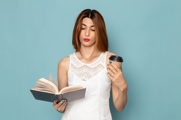 Frau im weißen Kleid hält Kaffeetasse und liest ein Buch