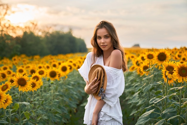 Frau im weißen Sommerkleid posiert auf Sonnenblumenfeld