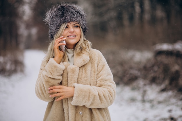Frau im Wintermantel, die im Park voller Schnee spaziert und am Telefon spricht