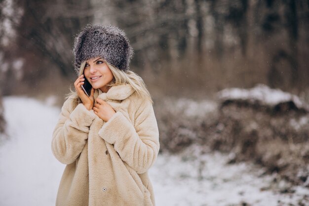 Frau im Wintermantel, die im Park voller Schnee spaziert und am Telefon spricht