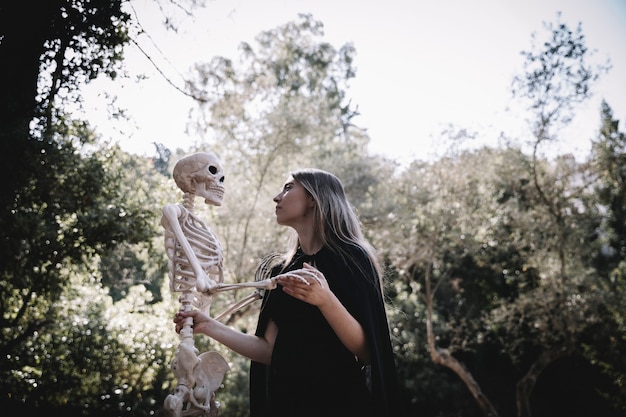 Frau im Zauberer kleidet das Schauen auf Skelett aufmerksam