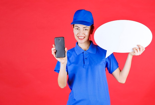 Frau in blauer Uniform, die ein ovales Ideenbrett hält und ein Mobiltelefon hält.