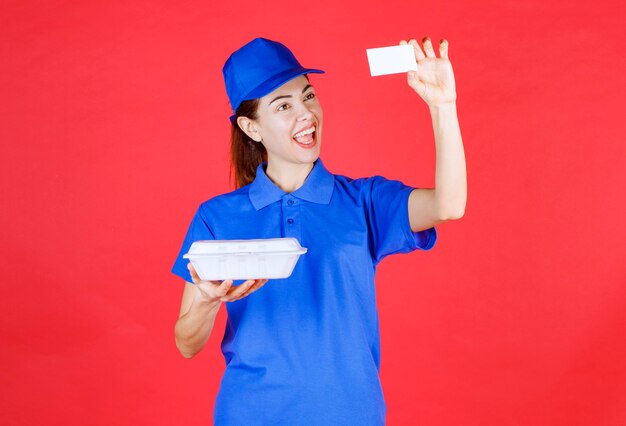 Frau in blauer uniform, die eine weiße plastikbox zum mitnehmen hält und dem kunden ihre visitenkarte vorlegt.