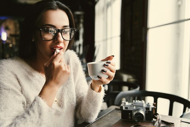 Frau in den Gläsern trinkt Kaffee und isst Zucker am Tisch im hellen Café