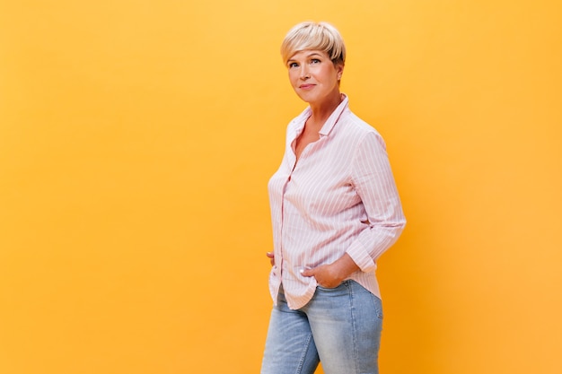 Frau in den Jeans und im Hemd wirft auf orange Hintergrund auf