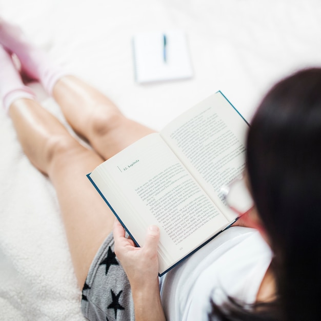 Frau in den Pyjamas, die auf Bett lesen