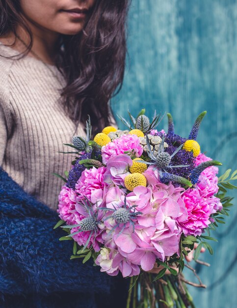 Frau in der beige Strickjacke mit einem Mischblumenblumenstrauß.