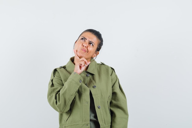 Frau in der Jacke, T-Shirt, das Finger am Kinn hält und nachdenklich schaut