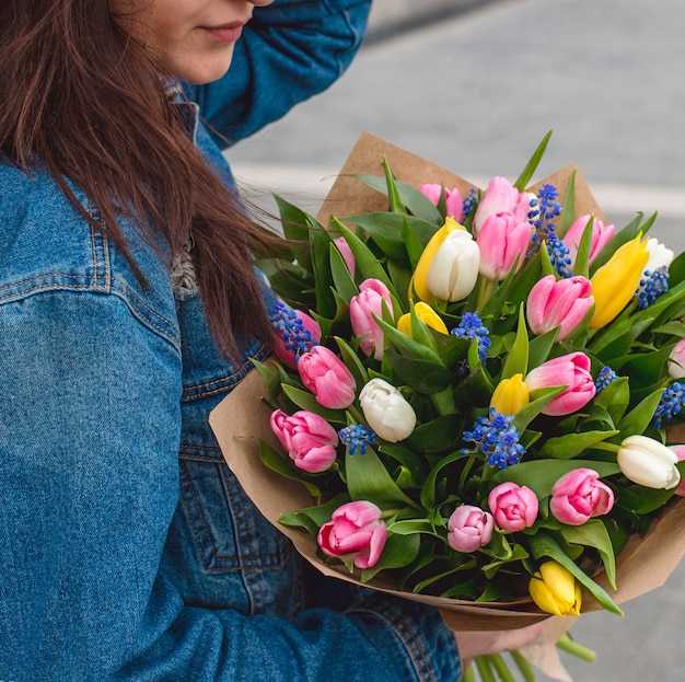 Frau in der Jeansjacke mit einem Blumenstrauß von bunten Tulpen.