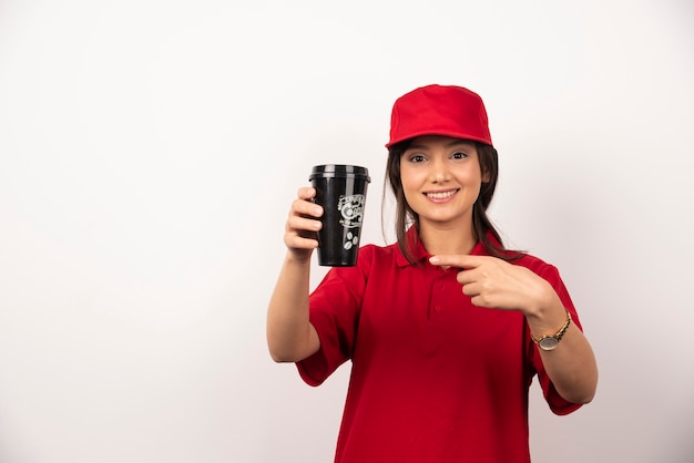 Frau in der roten Uniform, die eine Tasse Kaffee auf weißem Hintergrund zeigt.