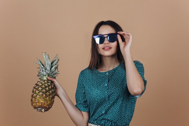 Frau in der schwarzen Sonnenbrille wirft mit einer Ananas im Studio auf