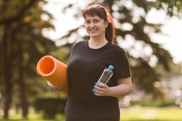 Frau in der Sportbekleidung, die eine Yogamatte und eine Flasche Wasser hält