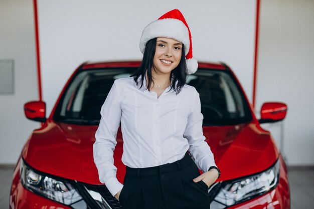 Frau in der Weihnachtsmütze durch das rote Auto in einem Autohaus