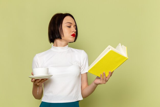 Kostenloses Foto frau in der weißen bluse und im grünen rock hält tasse tee und liest ein buch