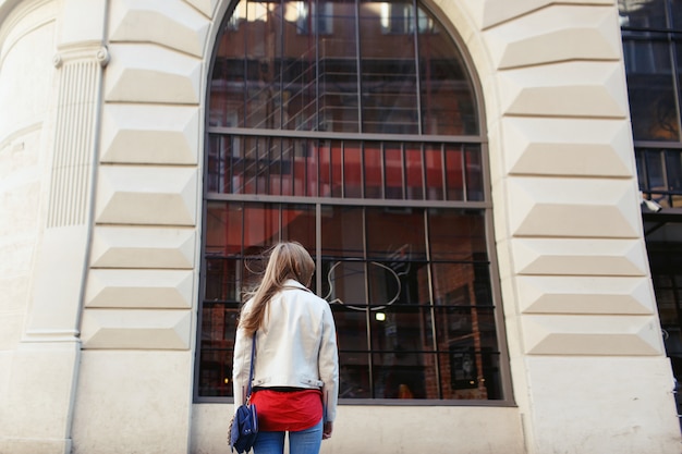 Frau in der weißen Jacke steht vor einem Fenster auf der Straße