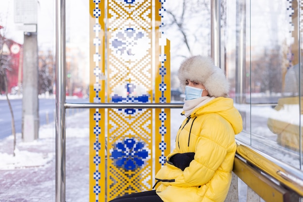 Kostenloses Foto frau in der winterkleidung an einem kalten tag, der an einer bushaltestelle auf einen bus wartet