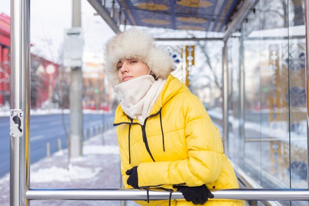 Frau in der Winterkleidung an einem kalten Tag, der an einer Bushaltestelle auf einen Bus wartet