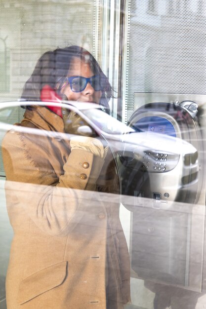 Frau in einem Anruf in einer Glastelefonzelle mit einem Spiegelbild eines Autos auf der Straße