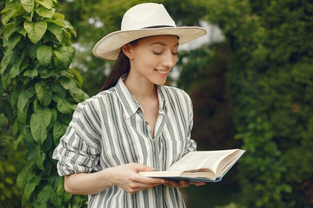 Frau in einem Hut mit einem Buch in einem Garten
