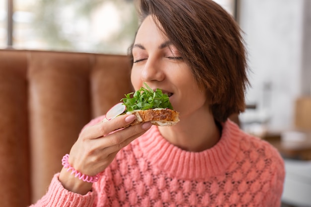 Frau in einem restaurant in einem gemütlichen warmen pullover gesundes frühstück mit toast mit rucola und lachs