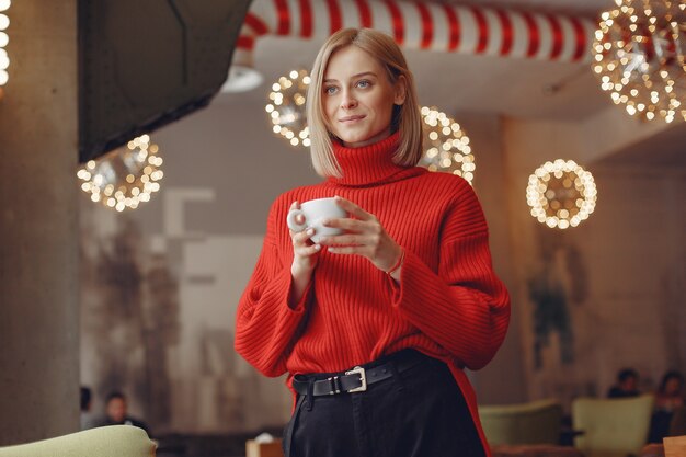 Frau in einem roten Pullover. Dame trinkt einen Kaffee.