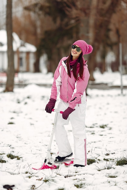 Frau in einem Winterpark. Dame im rosa Sportanzug. Frau mit Schneescooter.