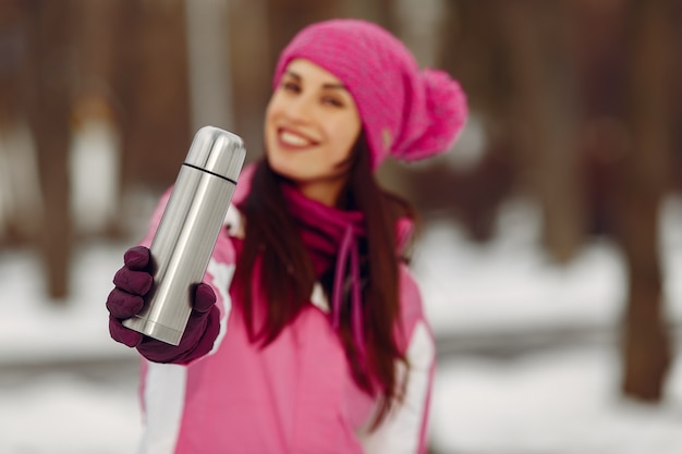 Frau in einem Winterpark. Dame im rosa Sportanzug. Mädchen mit einer Thermoskanne.