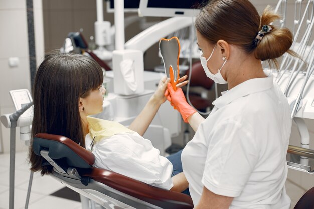 Frau in einem Zahnarztstuhl. Mädchen schaut in den Spiegel. Schönheit behandelt ihre Zähne