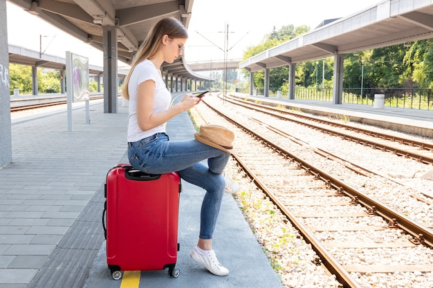 Frau in einer Bahnstation, die auf einem Gepäck sitzt