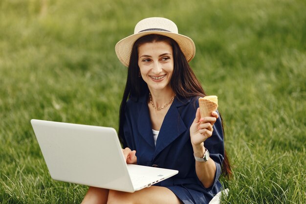 Frau in einer Frühlingsstadt. Dame mit einem Laptop. Mädchen sitzt auf einem Gras.