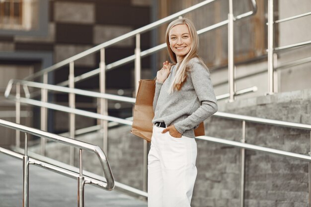 Frau in einer Sommerstadt. Dame mit braunen Taschen. Frau in einem grauen Pullover.