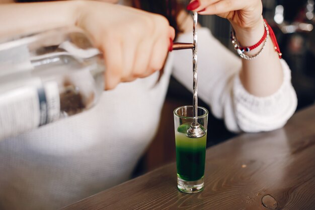 Frau in einer weißen Strickjacke, die grüne Spritze in Glas gießt