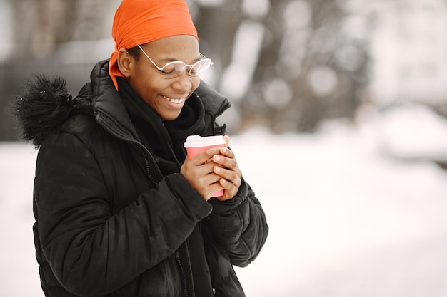 Frau in einer Winterstadt. Mädchen in einer schwarzen Jacke. Afrikanerin mit Kaffee.