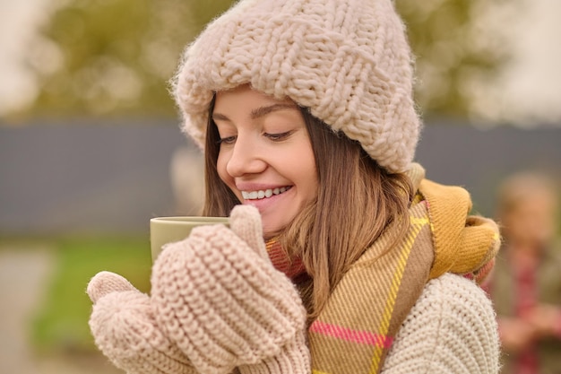 Frau in gestrickter Kleidung, die mit Freude in die Tasse schaut