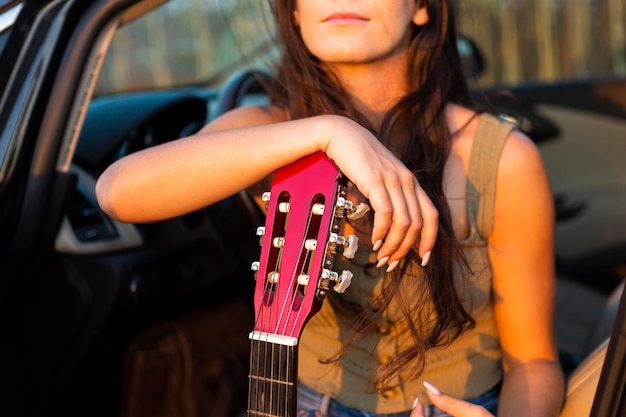 Kostenloses Foto frau in ihrem auto, das sonnenuntergang bewundert, während auf gitarre ruht
