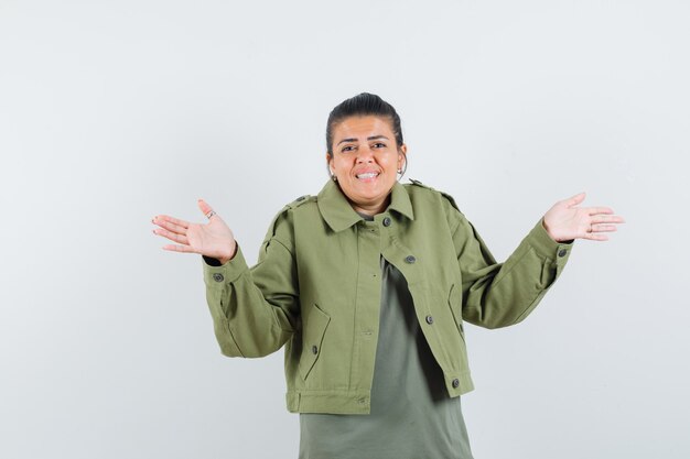 Frau in Jacke, T-Shirt zeigt hilflose Geste und sieht optimistisch aus