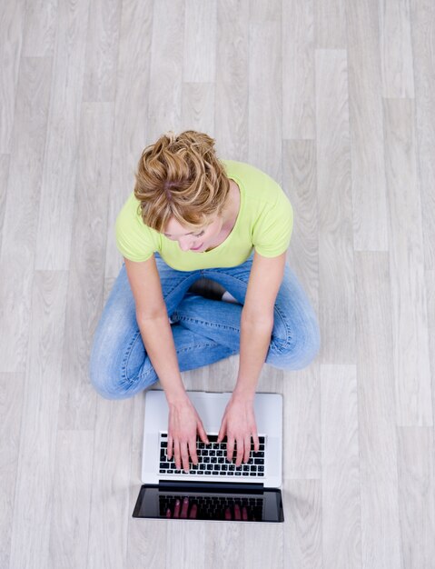 Frau in lässigen Sitzen auf dem Boden mit Laptop - High Angle Shoot