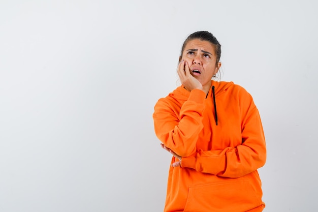 Frau in orangefarbenem Hoodie, die das Kinn auf die Hand stützt und nachdenklich aussieht