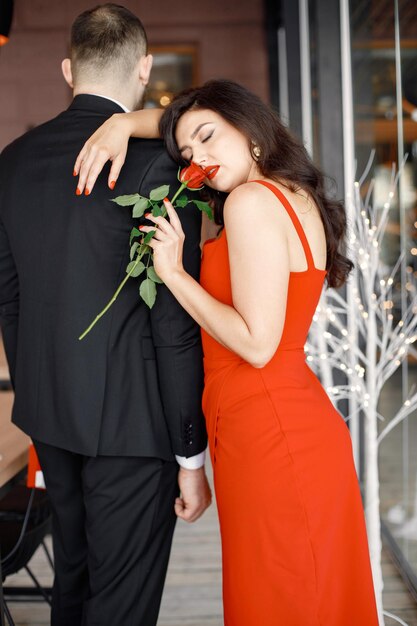 Frau in rotem, elegantem Kleid, die im Restaurant steht und ihren Freund umarmt