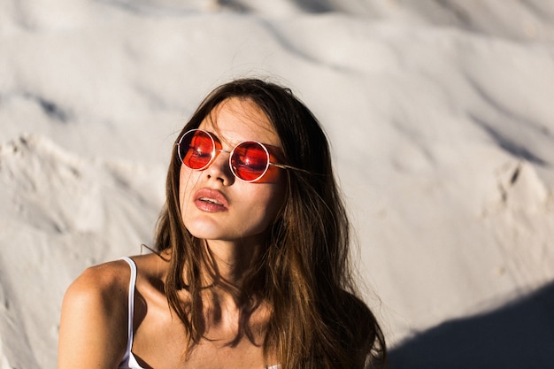 Frau in roten Sonnenbrillen liegt an einem weißen Strand