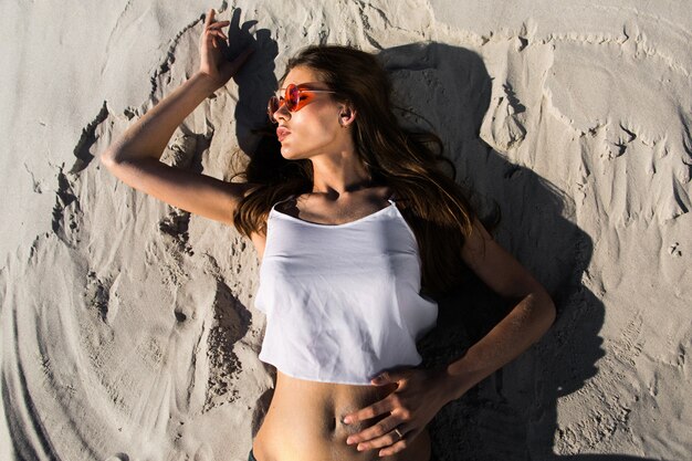 Frau in roten Sonnenbrillen liegt an einem weißen Strand