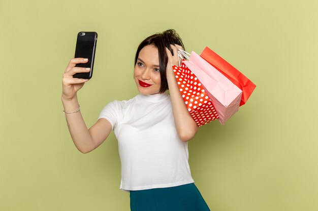 Frau in weißer Bluse und grünem Rock hält Einkaufspakete und macht ein Selfie