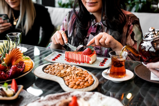 Frau isst Erdbeerkäsekuchen serviert mit Tee