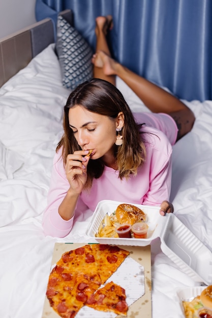 Frau isst Fast Food auf dem Bett