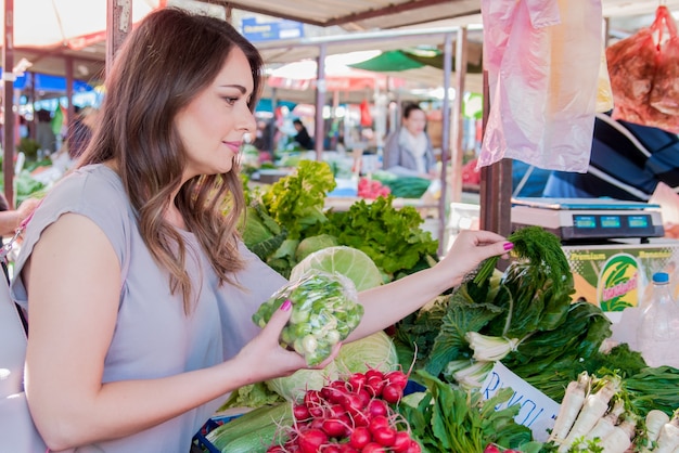 Frau kauft frisches Bio-Gemüse am Straßenmarkt. Lächelnde Frau mit Gemüse auf Marktgeschäft. Konzept der gesunden Lebensmittel einkaufen